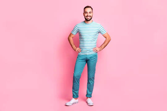 a man standing in front of a pink wall with his hands on hips and a big smile