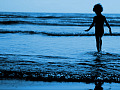 young boy standing in the water at the edge of the waves rippling in